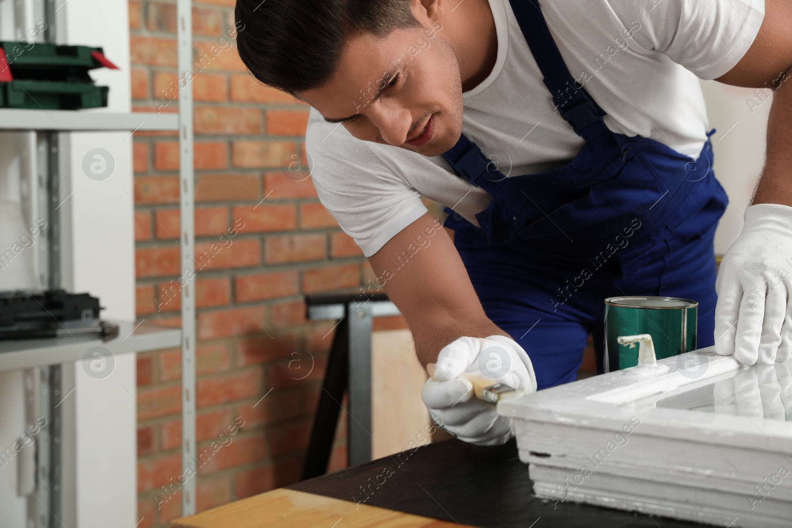 Photo of Repairman painting old window at table indoors