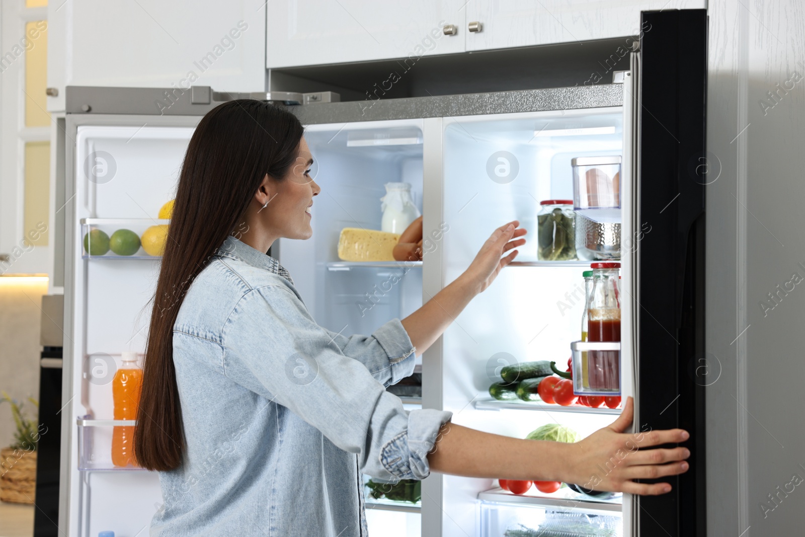 Photo of Young woman near modern refrigerator in kitchen