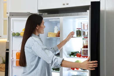 Young woman near modern refrigerator in kitchen