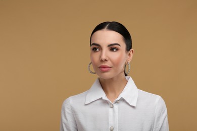 Photo of Beautiful young woman with elegant earrings on beige background