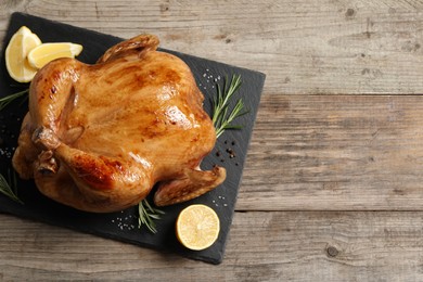 Tasty roasted chicken with spices and lemon on wooden table, top view. Space for text