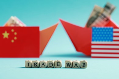 Photo of Phrase Trade war made of wooden cubes near paper boats with money and national flags on turquoise background