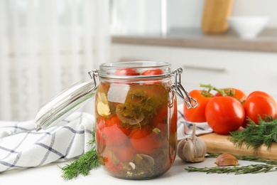 Photo of Pickled tomatoes in glass jar and products on white table in kitchen
