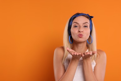 Photo of Portrait of hippie woman blowing kiss on orange background. Space for text