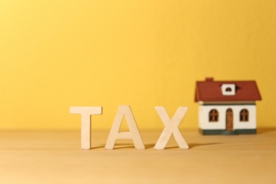Photo of Word TAX and house model on table against color background