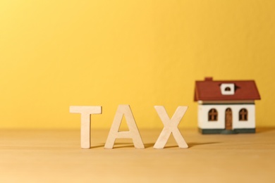 Word TAX and house model on table against color background