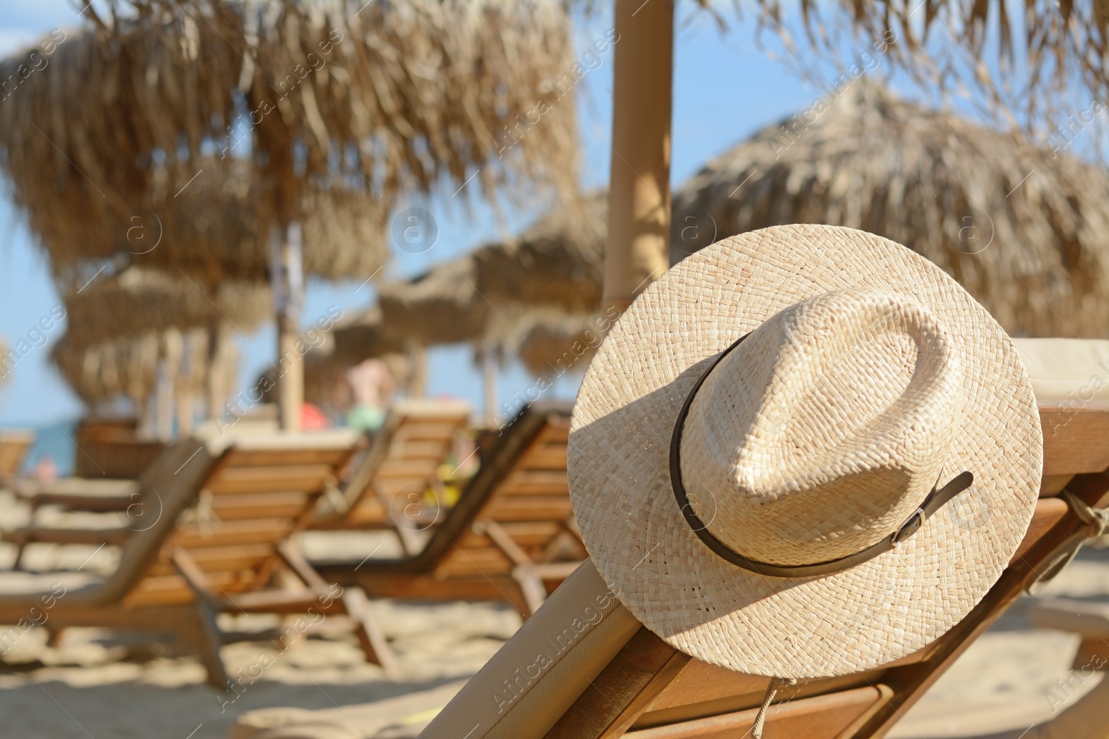 Photo of Stylish straw hat on wooden sunbed at beach, space for text