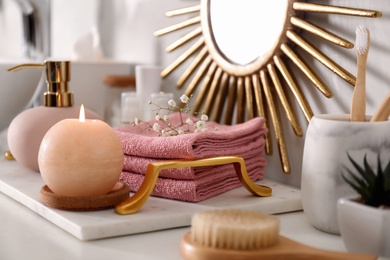 Photo of Tray with burning candle, soap dispenser and towels on countertop in bathroom