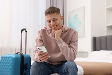 Smiling guest with smartphone relaxing on bed in stylish hotel room