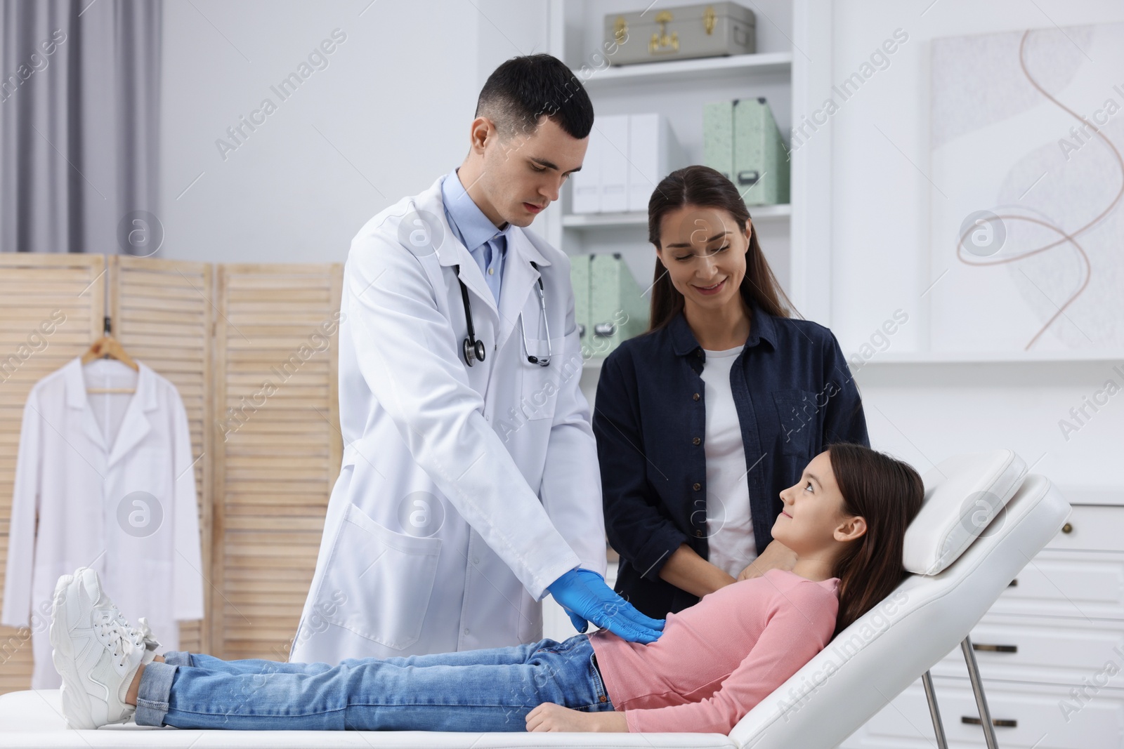 Photo of Gastroenterologist examining girl with stomach ache on couch in clinic