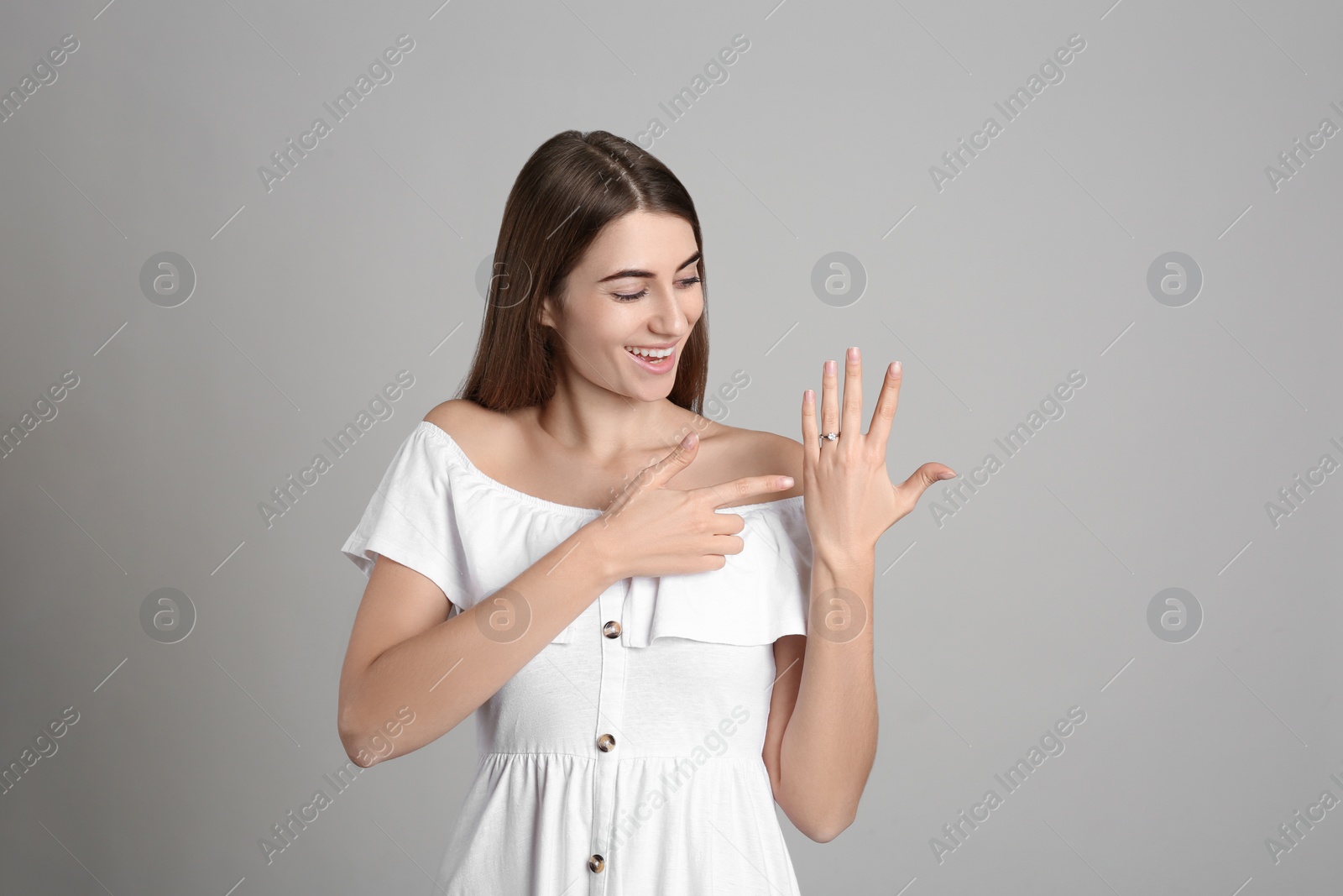 Photo of Happy young woman wearing beautiful engagement ring on grey background