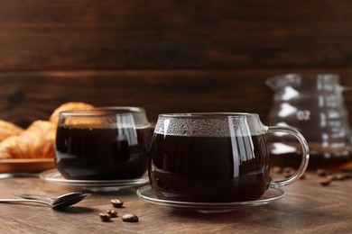 Photo of Hot coffee in glass cups, spoons and beans on wooden table, closeup