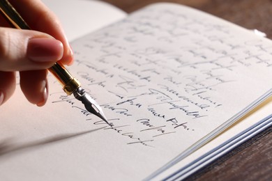 Photo of Woman writing with fountain pen in notebook at table, closeup