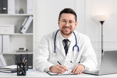 Photo of Smiling doctor working at table in clinic. Online medicine