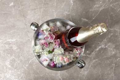 Photo of Bottle of champagne with floral ice cubes in bucket on table, top view