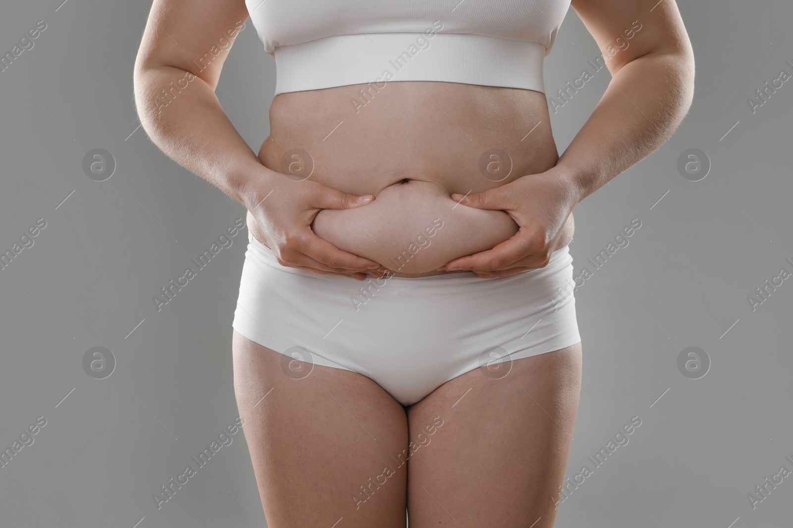 Photo of Woman touching belly fat on grey background, closeup. Overweight problem