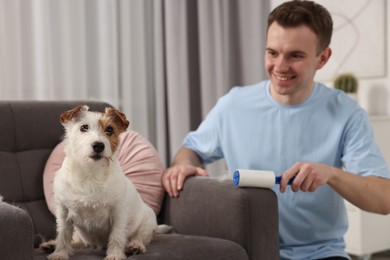 Photo of Smiling man removing pet's hair from armchair at home, selective focus