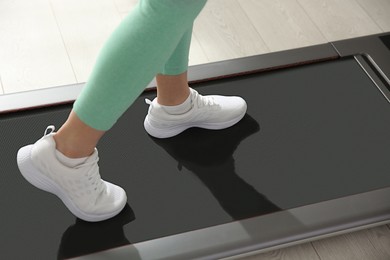 Photo of Sporty woman training on walking treadmill indoors, closeup