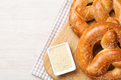 Photo of Delicious pretzels and bowl with sesame seeds on white wooden table, flat lay. Space for text