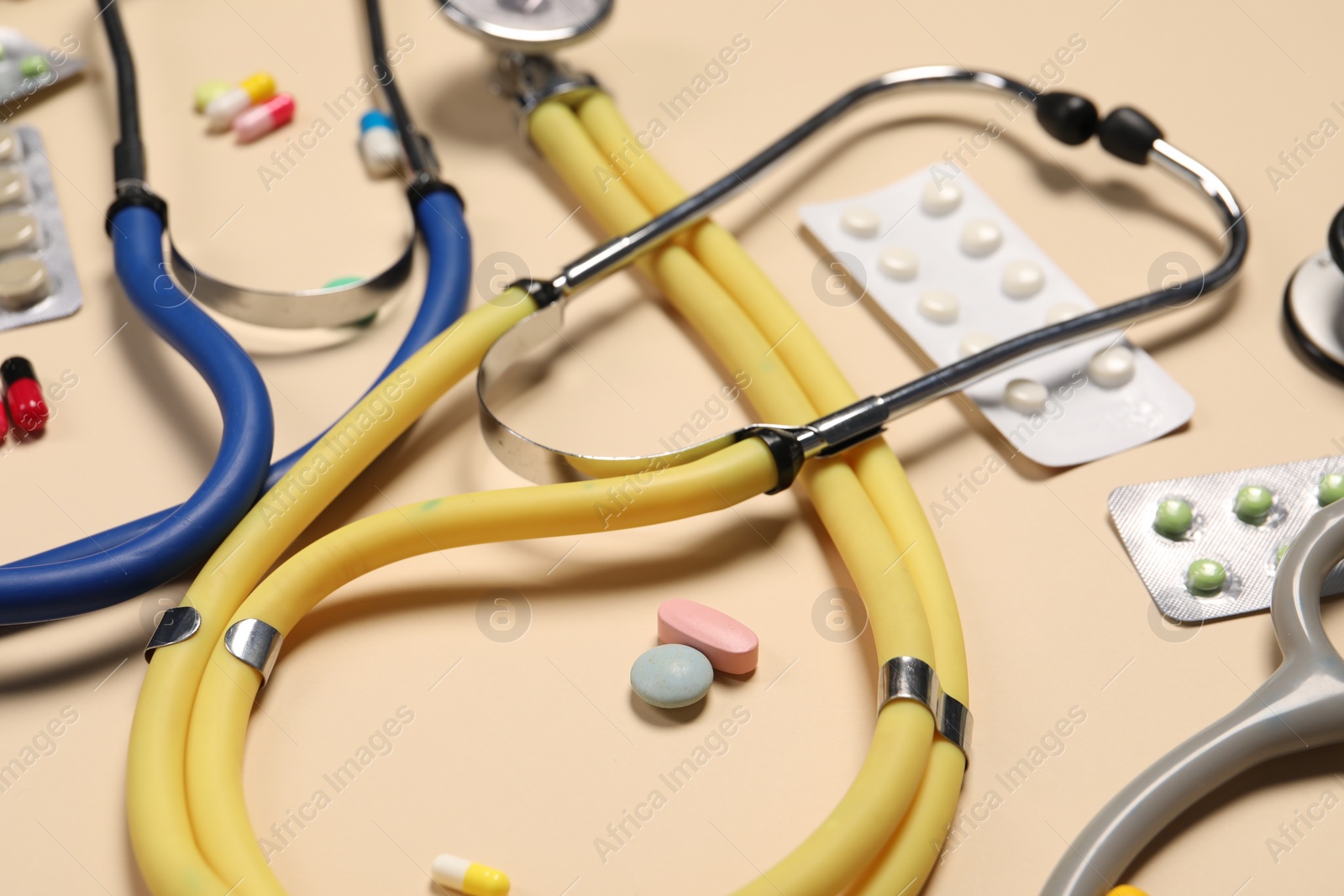 Photo of Stethoscopes and pills on beige background, closeup. Medical tools