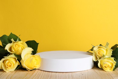 Photo of Beautiful presentation for product. White round podium and roses on wooden table against yellow background, space for text