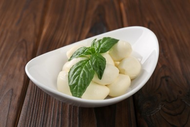 Tasty mozarella balls and basil leaves in bowl on wooden table, closeup