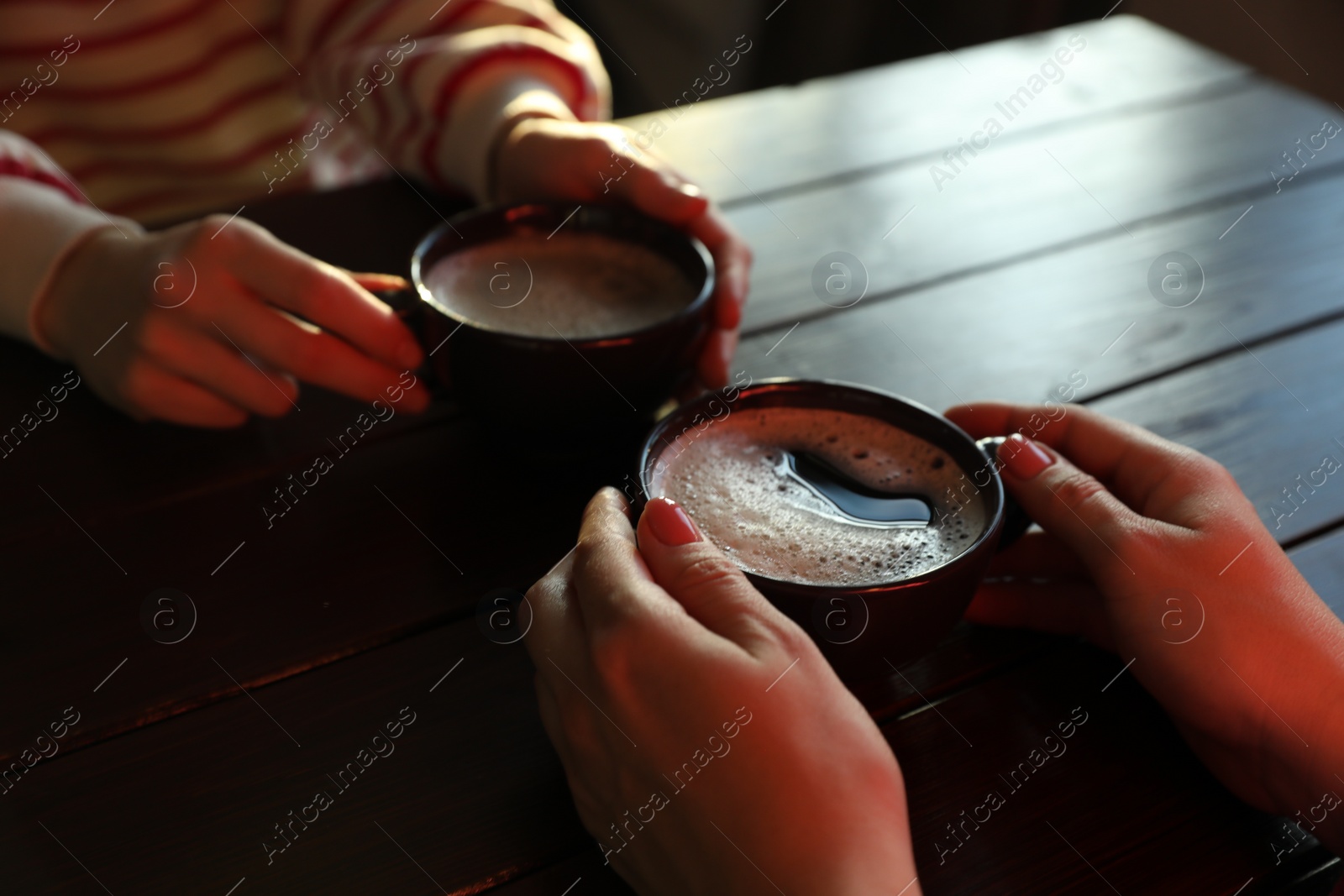 Photo of Women with cups of hot coffee at wooden table, closeup