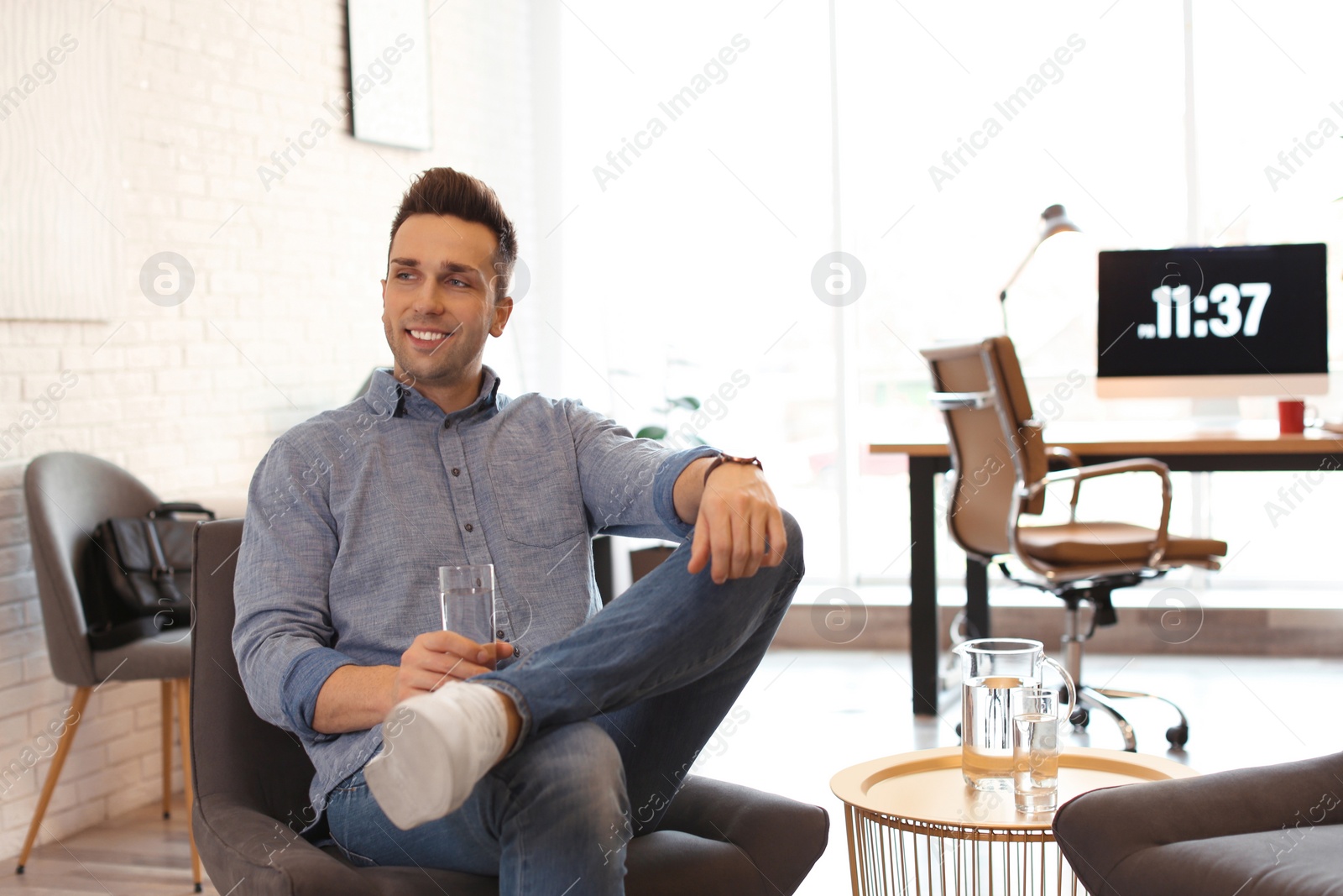 Photo of Young man with glass of water relaxing in comfortable chair at workplace