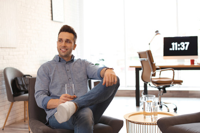 Photo of Young man with glass of water relaxing in comfortable chair at workplace