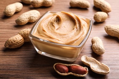 Photo of Yummy peanut butter in glass bowl on wooden table, closeup