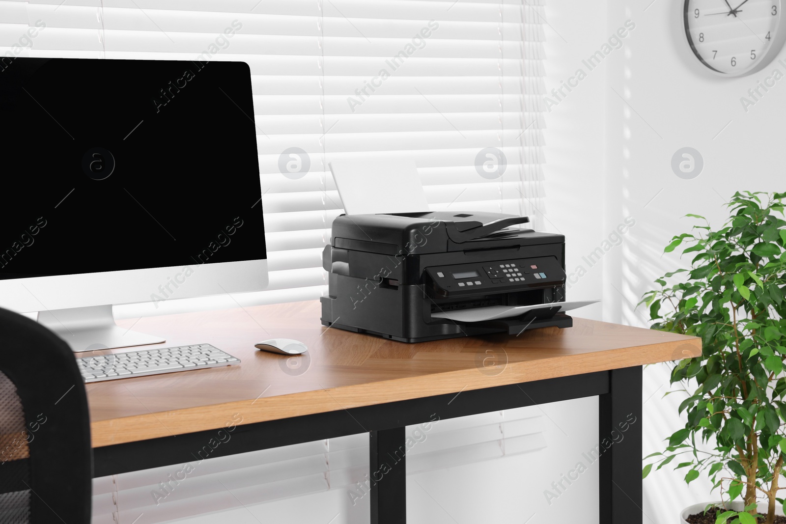 Photo of Modern printer with paper near computer on wooden table in home office