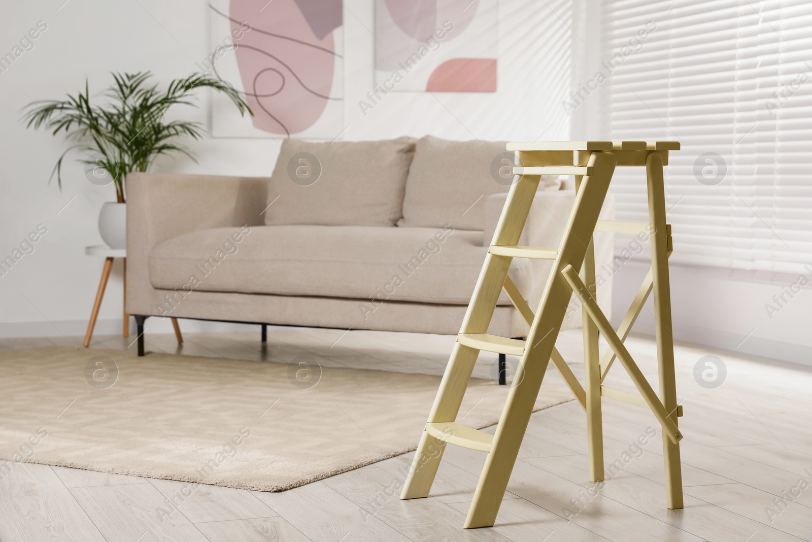 Photo of Folding ladder near sofa on wooden floor at home