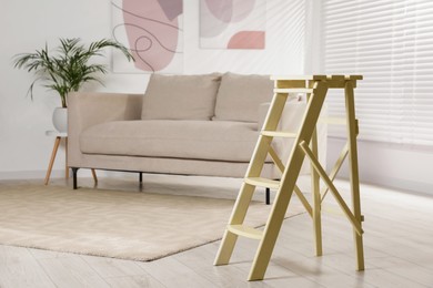 Photo of Folding ladder near sofa on wooden floor at home