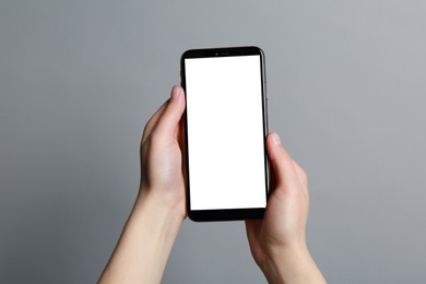 Woman holding smartphone with blank screen on grey background, closeup. Mockup for design