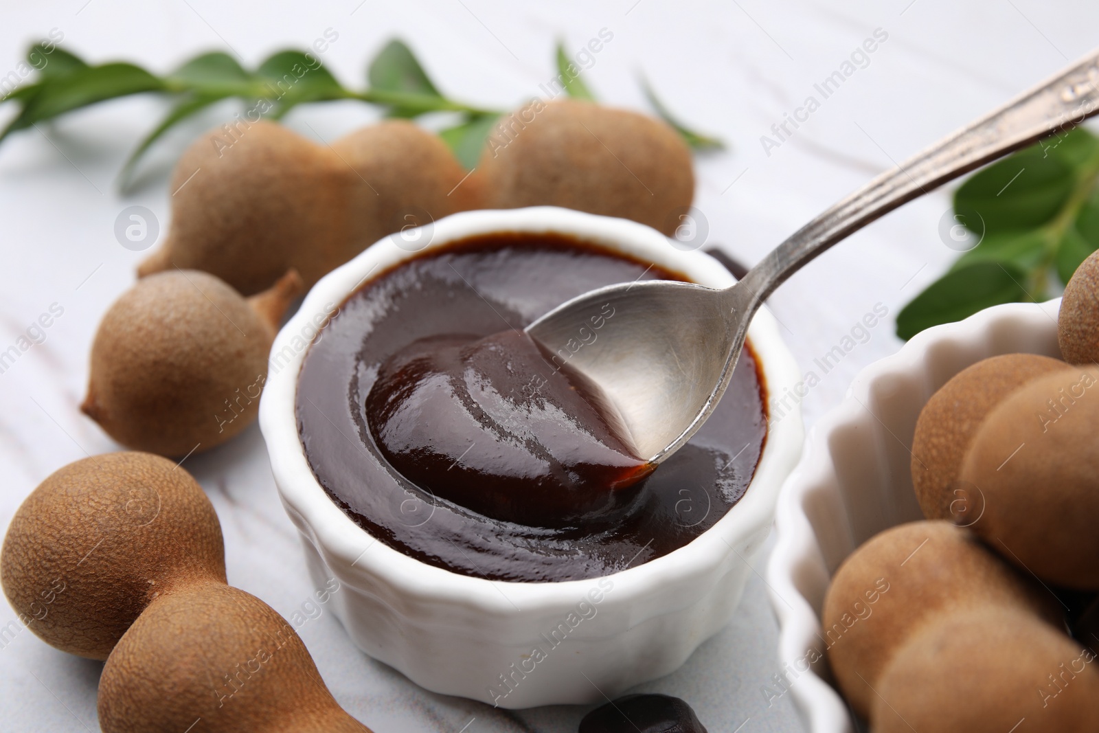 Taking tasty tamarind sauce with spoon from bowl on table, closeup Photo of Taking tasty tamarind sauce with spoon from bowl on table, closeup