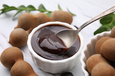 Photo of Taking tasty tamarind sauce with spoon from bowl on table, closeup