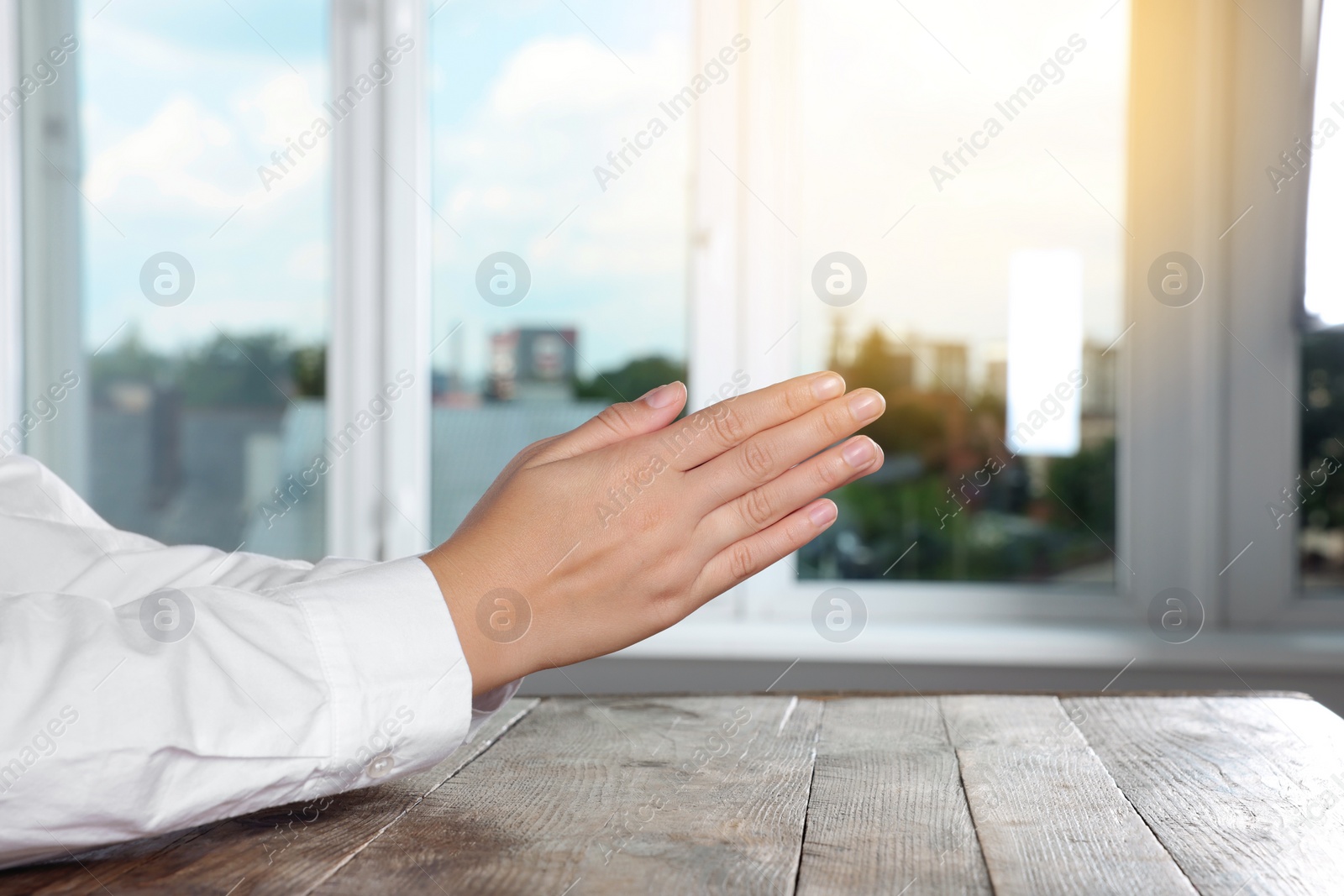 Photo of Woman holding hands clasped while praying at wooden table near window, closeup