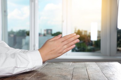 Photo of Woman holding hands clasped while praying at wooden table near window, closeup