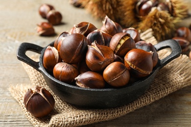 Photo of Tasty roasted edible chestnuts on wooden table, closeup