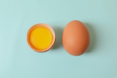 Cracked and whole chicken eggs on light blue background, flat lay