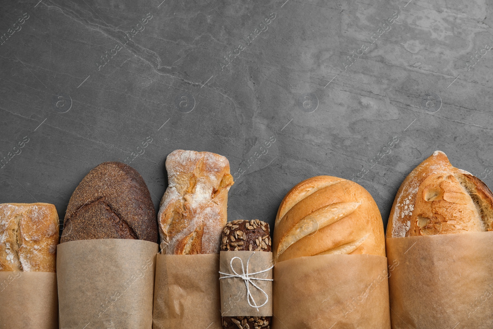 Photo of Different kinds of fresh bread on grey table, flat lay. Space for text