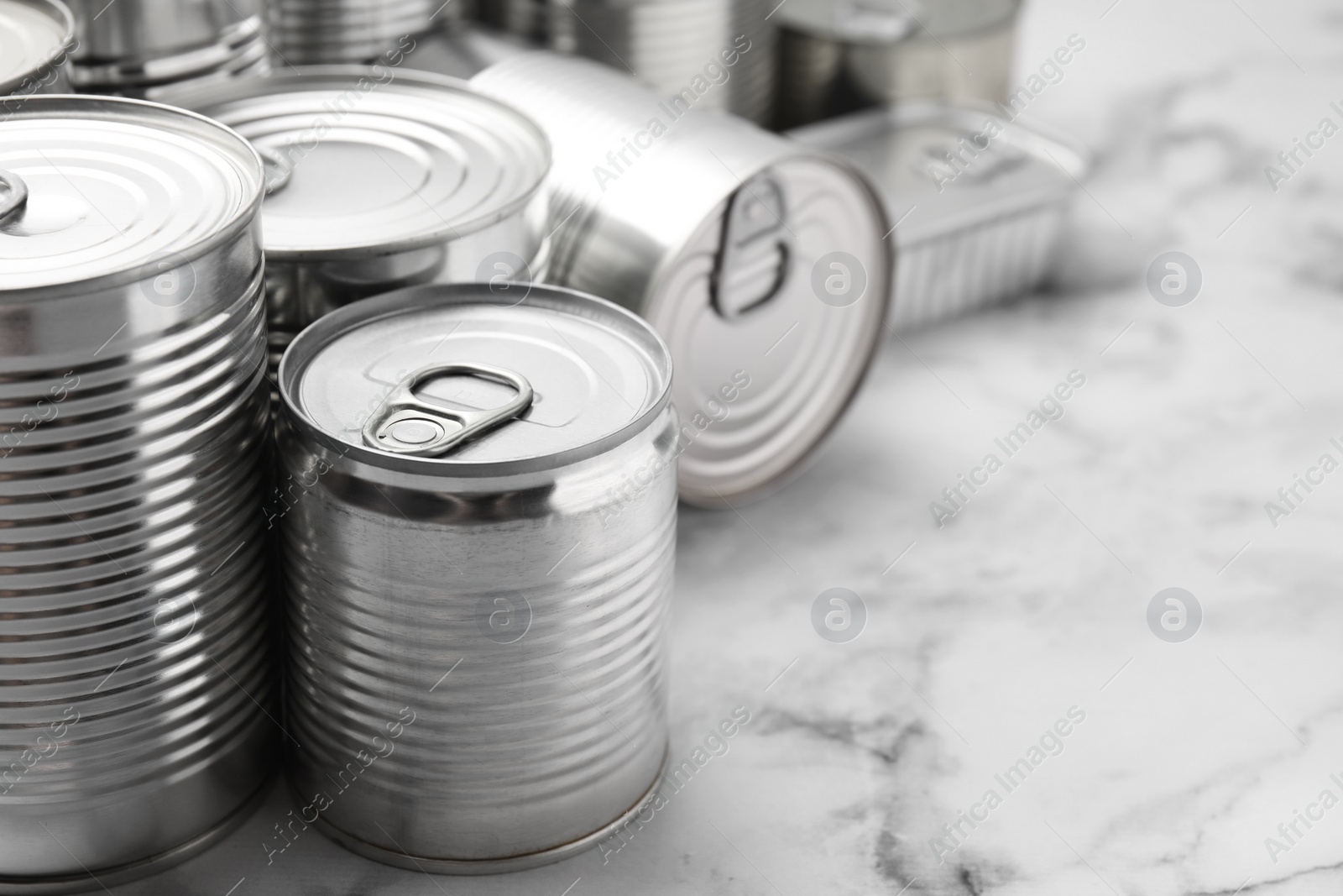 Photo of Many closed tin cans on white marble table, closeup. Space for text