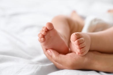 Photo of Mother holding feet of her little baby on bed, closeup. Space for text
