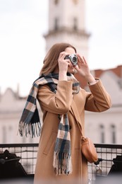 Beautiful woman in warm scarf taking picture with vintage camera outdoors