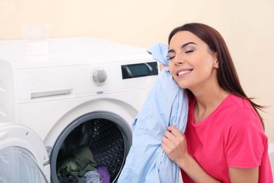Photo of Young woman with clean laundry near washing machine at home