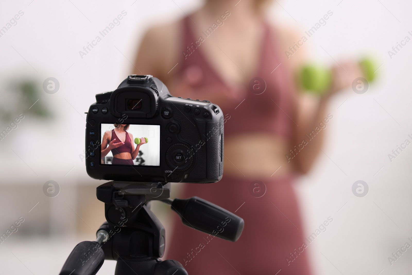 Photo of Sports blogger with dumbbell recording fitness lesson at home, focus on camera. Space for text