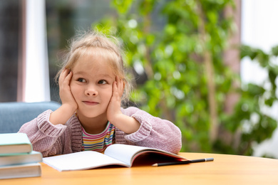 Photo of Cute little girl studying at wooden table indoors. Space for text