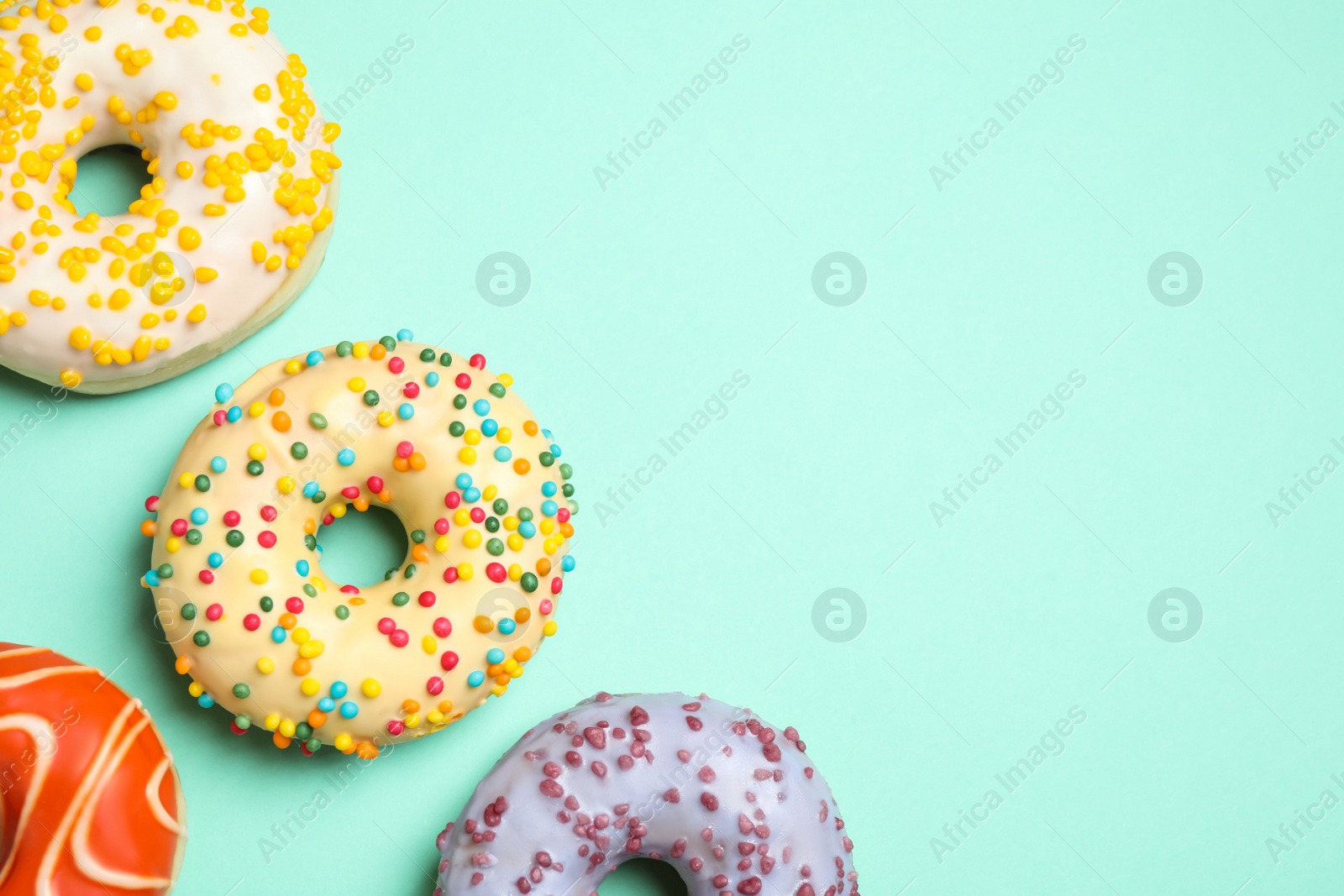 Photo of Delicious glazed donuts on turquoise background, flat lay. Space for text