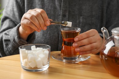 Woman adding sugar cube into aromatic tea at wooden table, closeup