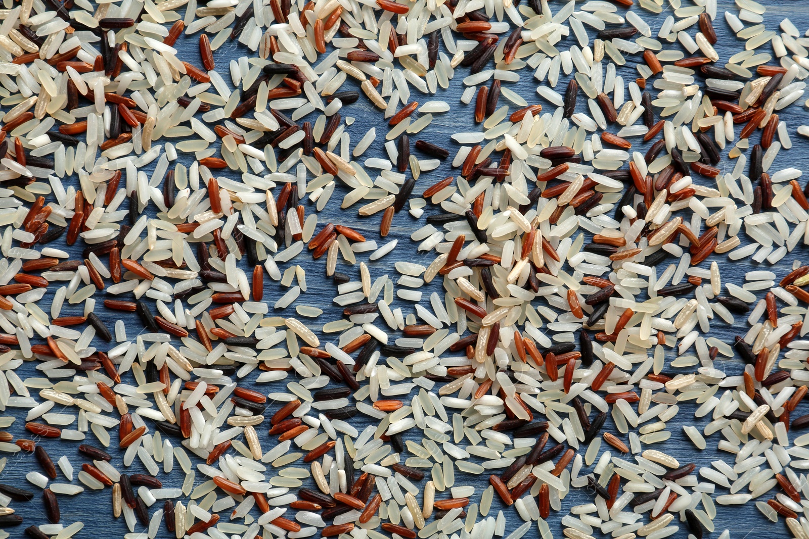 Photo of Brown and other types of rice scattered on color wooden background